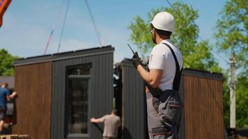 Construction foreman communicating with walkie talkie during prefabricated house installation video
