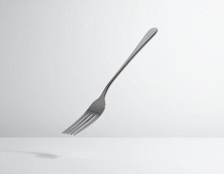 A single, shiny silver fork rests on a white surface, casting a subtle shadow. photo