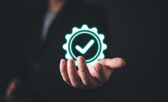 A businessman extends his hand, displaying a glowing quality assurance icon with a checkmark inside a gear. The image symbolizes certification, control, and adherence to industry standards. photo