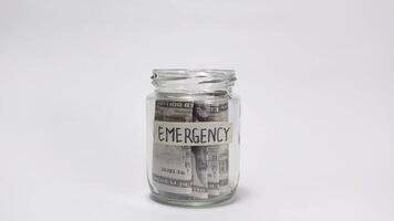 en hand placering dollar räkningar in i en burk märkt nödsituation, symboliserar finansiell besparingar, beredskap, och de betydelse av byggnad en säkerhet netto för oväntat situationer. video