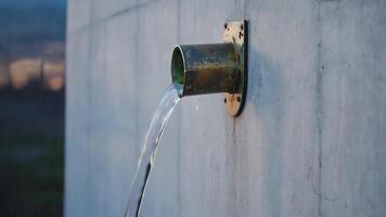 A minimalist, abstract shot of a single, thin stream of water flowing from a gutter pipe, with raindrops falling into it video