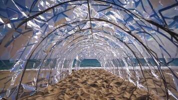 transparent archway strukturera på sandig strand, visa upp skimrande reflektioner och hav se, skapande en fängslande visuell resa genom de kust landskap video