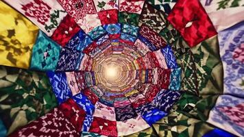 färgrik tyg mönster spiral inåt, skapande en fascinerande tunnel effekt upplyst förbi en ljus ljus på de Centrum, visa upp vibrerande texturer och invecklad mönster i rörelse video