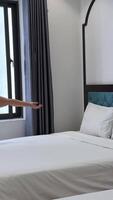 rechoncho mujer en a rayas vestir se sienta en cama se extiende brazos a lado mira fuera sucio ventana detrás cuales es turbio Mañana ver de pared de casa barato habitación para cuatro blanco hojas europeo mujer de años viajes video