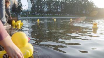 avvicinamento tiro cattura bambino accuratamente lancio giallo motorizzato anatra in scintillante acqua, ambientazione giocattolo in movimento come luce del sole punti salienti spruzzi e lontano anatre galleggiante nel sfondo. video