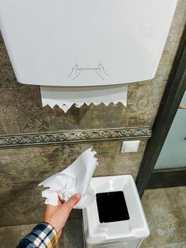 A person is in the process of taking a piece of paper towel out of a trash can that is meant for disposing of waste. This action can be considered quite unusual or surprising photo