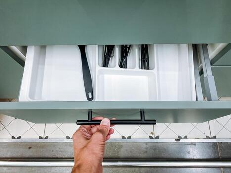 A person is currently in the process of opening a drawer that is filled with various utensils and kitchen tools, exploring the contents within for a specific item they need photo