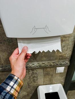 A person is methodically pulling a roll of multipurpose paper towels out of a specific paper towel dispenser designed for such products, which is often found in various establishments photo