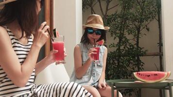 Chilling Asian family holidays, casual girl and mum in sunglasses enjoy drinking smoothie drinks and fresh watermelons sliced, happiness relaxing on vacation, and hot summertime at outdoor terrace. video