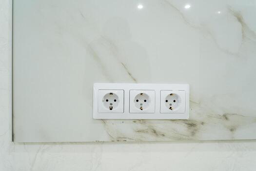 On a stunning marble wall, there are three white electrical outlets neatly installed, providing convenient access to power. These wall sockets are essential for connecting various devices photo