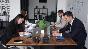 company employees in an open space office of different nationalities and genders work at computers with documents on the table video