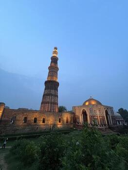 Upward perspective of the Qutub Minar showing architectural details against a cloudy sky photo