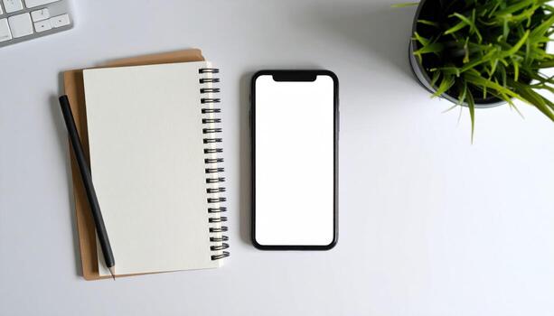 An open notebook with a blank page and a smartphone with a blank screen next to it, on a white desk with a pen and a plant. photo