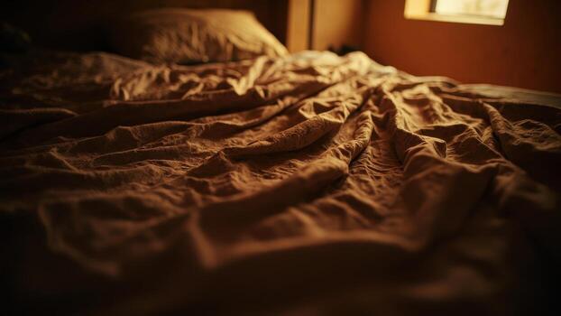 Unmade bed with crumpled brown sheets and pillow illuminated by natural light from a window creating a warm glow. photo