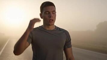 erschöpft jung männlich Athlet nehmen sich ausruhen und tief Atmung nach Joggen auf Asphalt Straße im nebelig Wetter unter Himmel während Sonnenaufgang video