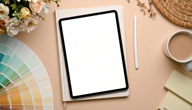 A top-down view of a tablet with a blank screen next to a color palette, flowers and stationery, photo