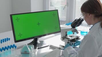 en fokuserade forskare i skyddande redskap undersöker prover under en mikroskop, medan en modern grön skärm övervaka förstärker de analys med digital överlägg för en Mer effektiv forskning bearbeta video