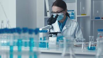 en tillägnad forskare i en vit labb täcka undersöker prover under en mikroskop, omgiven förbi Avancerad labb Utrustning, betona de betydelse av precision och noggrannhet i forskning video