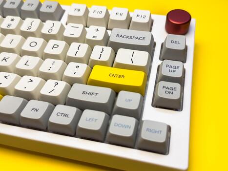 White mechanical keyboard with bright Enter key on bright yellow background, minimalism, keyboard buttons. A keyboard with a yellow key on the bottom left photo