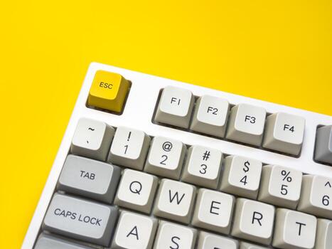 White mechanical keyboard with bright Esc key on bright background, office keyboard buttons. A keyboard with a yellow key on the bottom left photo