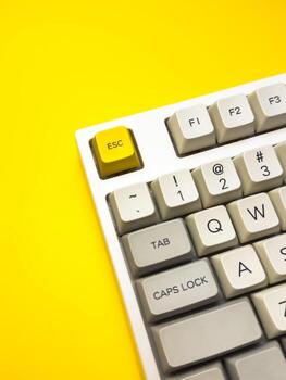 White mechanical keyboard with bright Esc key on yellow background minimalism, keyboard button photo