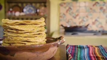 un' pila di tortillas nel un' argilla ciotola su un' tavolo nel un' cucina ambientazione con colorato Accenti nel il sfondo video