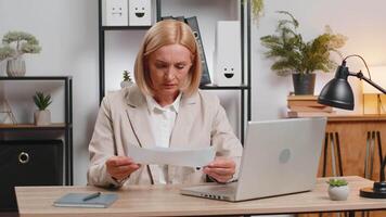 caucásico maduro mujer de negocios leyendo letras malo Noticias siente trastornado sentado a hogar oficina escritorio. financiero problemas, banco deuda cuenta para pagar, impuesto factura o bancarrota notificación. niña en formal traje video