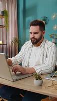 jovem homem empreendedor prepara comece projeto para apresentação encontra ideia. empregado trabalhador autonomo pensar digitando navegando usando computador portátil computador às casa escritório escrivaninha. controlo remoto distante trabalhando. vertical video