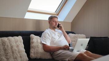 man talande på smartphone medan arbetssätt på bärbar dator på Hem video