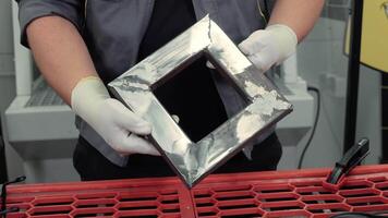 trabajador en protector guantes participación brillante cuadrado metal marco, pulido acero bordes con soldadura marcas visible a industrial taller mesa con rojo superficie video