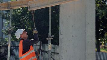 Construction worker in orange vest and white helmet pulling rope at concrete structure, active work process on building site with scaffolding and sunlight video