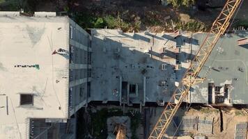 Aerial Top view of construction site with workers on reinforced concrete slab, visible crane arm and scattered equipment on unfinished building project video