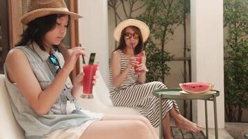 Asian family summer holidays, casual girl and mum enjoy eating pieces of fresh red watermelons sliced and smoothie drinks, happiness relaxing on vacation at outdoor terrace. video