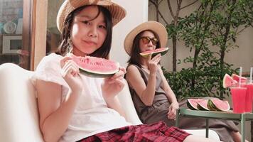 Asian family holidays, casual girl and mum enjoy eating pieces of fresh red watermelons sliced and smoothie drinks, happiness relaxing on vacation, and hot summertime at outdoor terrace. video