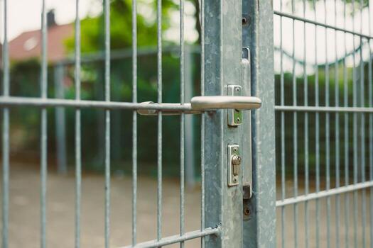 This is a CloseUp Image Featuring a Silver Metal Gate That Includes a Lock and Latch Mechanism, Surrounded by Lush Greenery Perfect for Visual Concepts Related to Security and Access Control photo