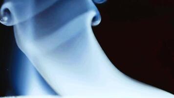 Real blue smoke rises and forms beautiful, intricate patterns in slow motion against a dark background. An elegant and mysterious abstract . video
