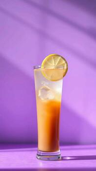 Refreshing orange drink with lemon slice and ice cubes on a purple background with shadow patterns photo