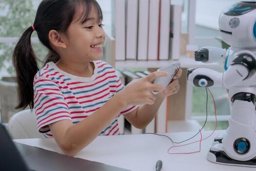 Asian girl smiling while controlling robot with smartphone at home, concept of STEM education, artificial intelligence, coding, and future technology learning for kids. photo