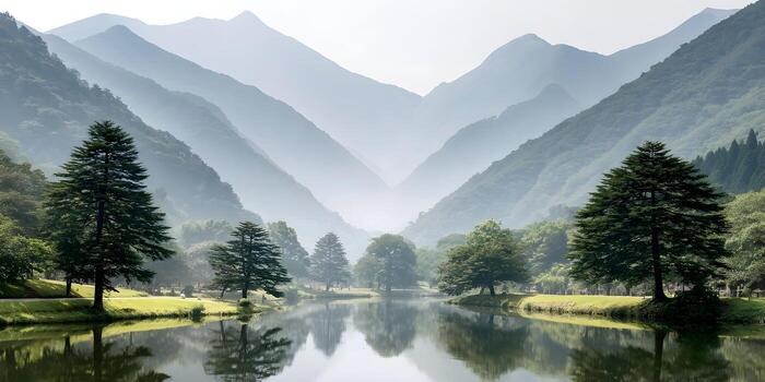 A tranquil lake reflects lush green trees and distant misty mountains under a clear sky photo