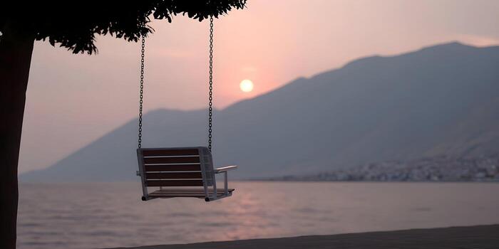 An empty swing hangs from a tree overlooking a calm ocean at sunset with mountains in the background photo