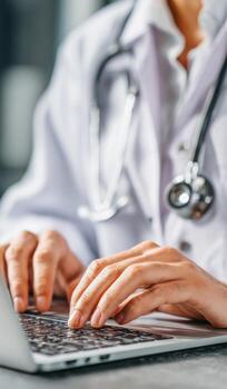 Doctor using laptop with stethoscope, medical professional typing on computer keyboard photo