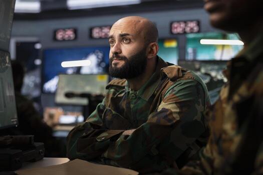 Special operations soldier looking at surveillance monitor, analyzing data to allocate resources to units based on mission needs. Agent examining strategic data on screen in military control center photo