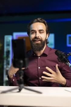 Online star talking in front on smartphone attached to tripod stabilizer in studio, discussing with viewers. Man using mobile phone to record in living room for social media photo