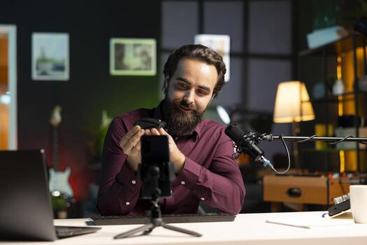 Content creator excited about newly launched wireless mouse, feeling impressed by high quality sensitivity. Joyful man trying out office computer peripheral, filming using smartphone on tripod photo
