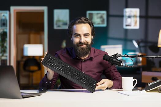 Smiling content creator filming keyboard review in personal studio, ready to start testing it. Cheerful technology guru showcasing computer peripheral to audience on niche online channel photo