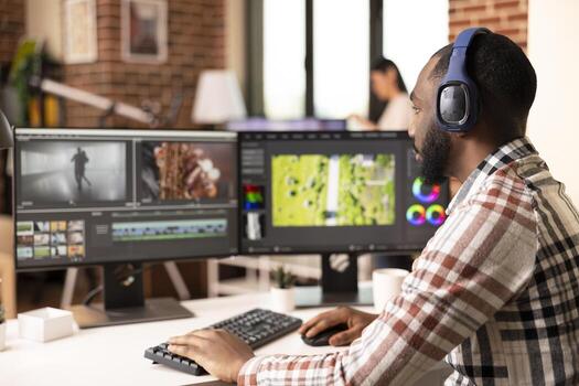 Focused sound editor with headphones using professional software, synchronizing audio tracks to visuals. Black man with two monitors, crafting cinematic content from raw clips at home studio. photo