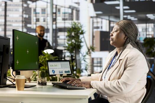 African american project manager working at desk next to copy space display, using performance metrics in order to review organizational success. Female analyst at workstation. photo