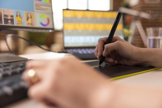 Closeup of hands working with stylus pen and drawing pad, enhancing photo content on desktop monitor and laptop. Productive editing workflow with digital devices in creative home studio.