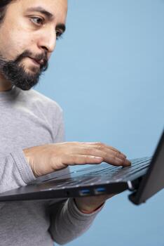 casual y confidente joven hombre utilizando un ordenador portátil en frente de el cámara, resolviendo independiente Tareas en línea. enfocado moderno persona lo hace digital trabajo o social redes en contra azul antecedentes. foto