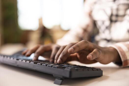 African American entrepreneur typing on computer keys to update reports and reply to emails. Black male remote worker using keyboard, inputting data and preparing online presentations at desk. photo